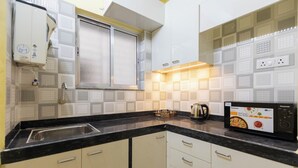 A kitchen with a black countertop, white cabinets, a built-in microwave, and a window above the sink. - City Haven by Jadecaps Nr. Belle Vue Hsp 3bhk (Kolkata)