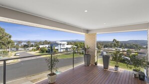 A balcony with a view of a road and houses, featuring a wooden floor and potted plants. - Beautiful House with Mountain and Water Views and Kangaroos. (Long Beach)