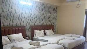 A hotel room with three beds, each with white linens and towels, a wooden headboard, and a forest-themed wallpaper. - Skyline Residency (Bengaluru)