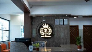 A reception desk with a logo, a computer, a plant, and a window with a view of buildings. - Skyline Residency (Bengaluru)