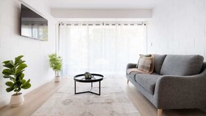 Un salon moderne avec un canapé gris, une table basse ronde et deux plantes en pot.