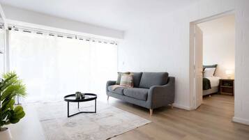 A modern living room with a grey sofa, a round coffee table, and a large window with curtains.
