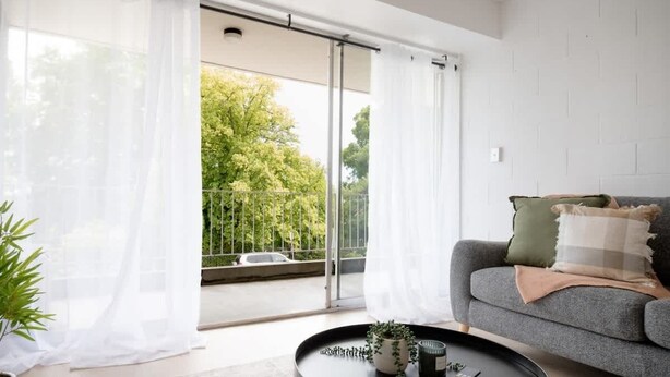 Un salon moderne avec un canapé gris, une table basse ronde agrémentée d’une plante, et une vue sur l’extérieur à travers une porte vitrée.