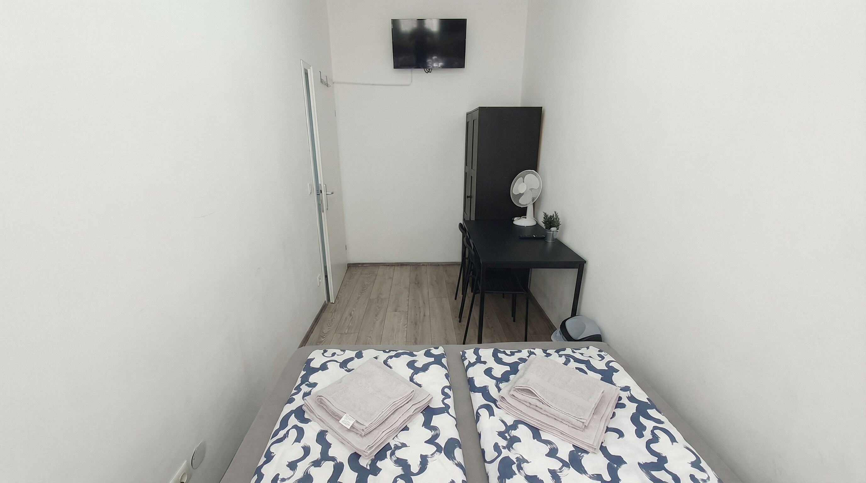 Een kleine kamer met twee bedden, een bureau, een stoel, een televisie en een ventilator.