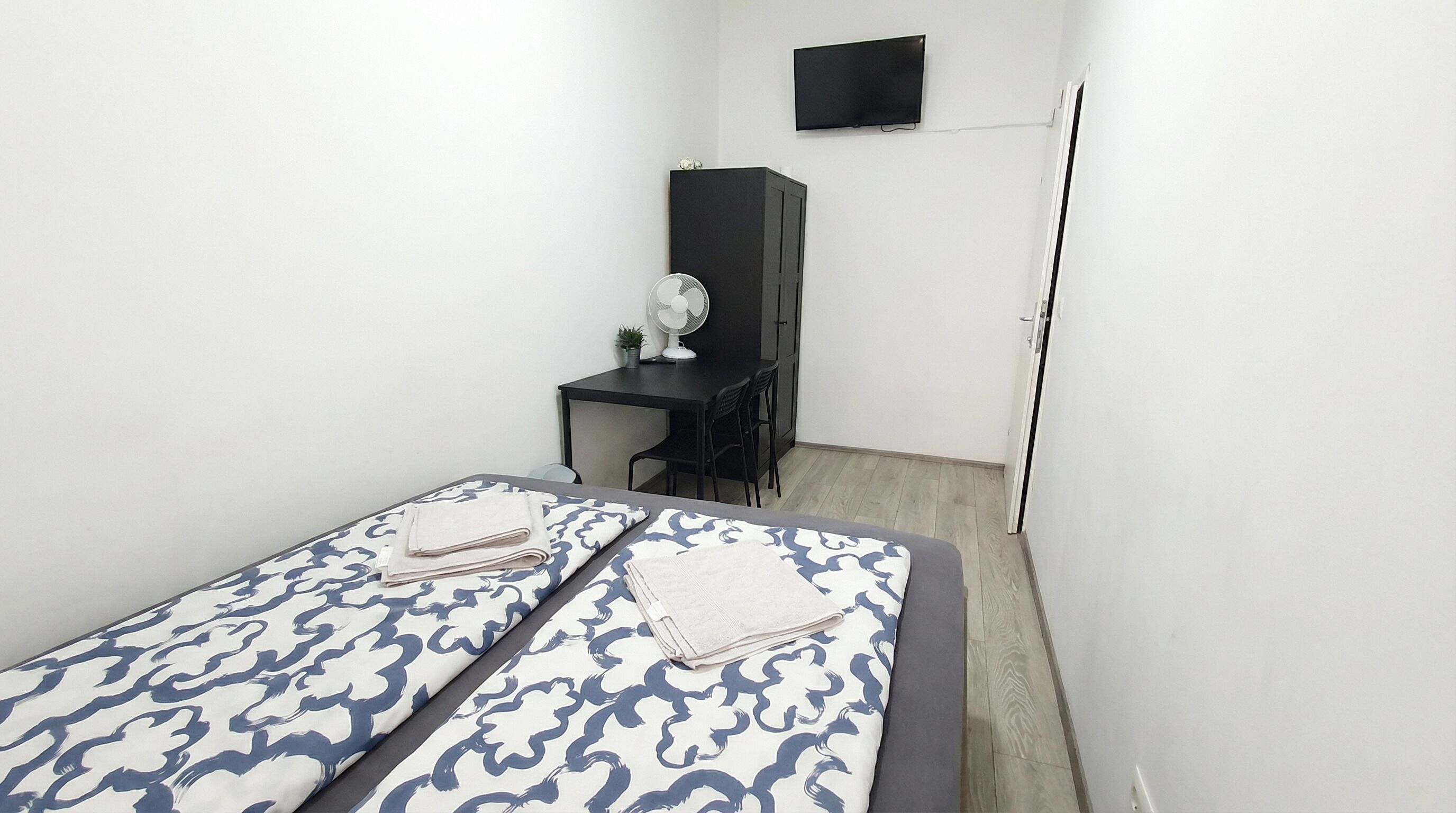 A small, clean room with a bed, a desk, a chair, a TV, and a wardrobe.
