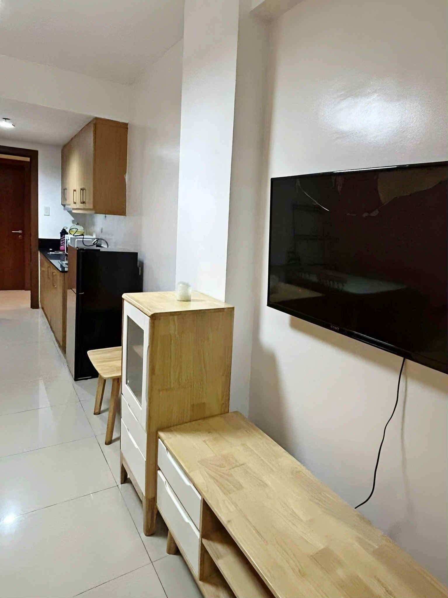 Un espacio habitable compacto con kitchenette, un televisor montado en la pared y un banco de madera.