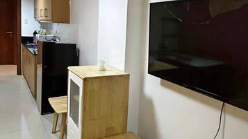 Un espacio habitable compacto con kitchenette, un televisor montado en la pared y un banco de madera.
