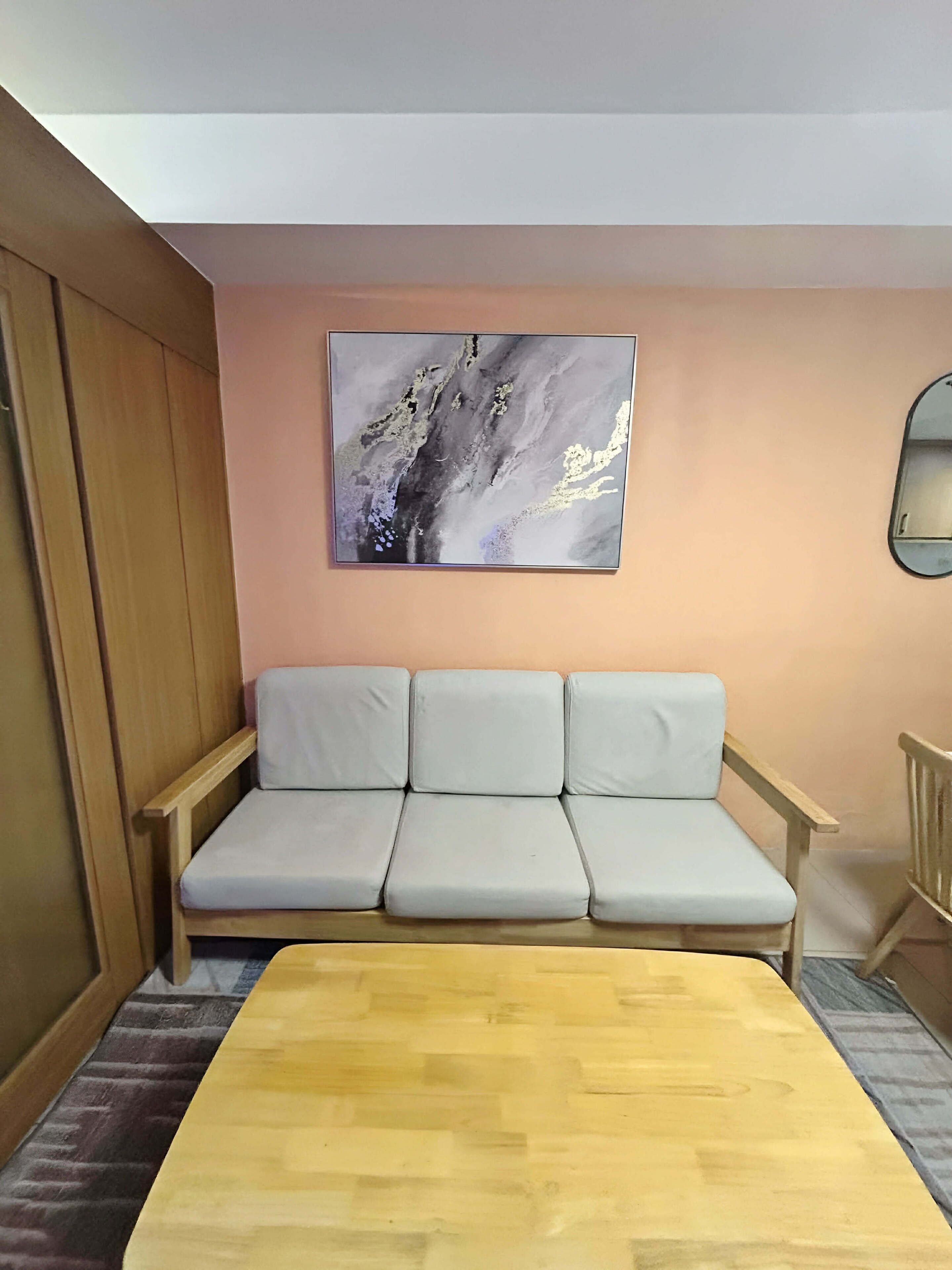 A room with a wooden floor, a grey sofa, a wooden table, and a wall-mounted painting.