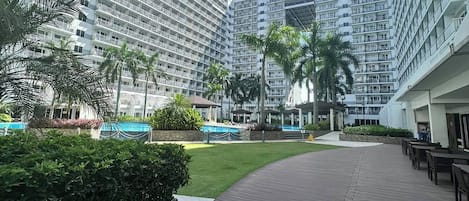 A modern hotel with multiple high-rise buildings, a central courtyard with palm trees, and a covered outdoor seating area.