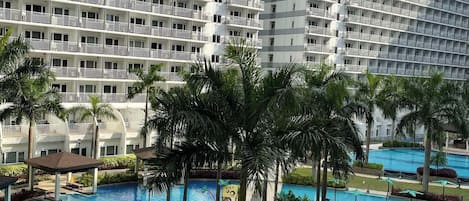 A large hotel with multiple balconies and a central swimming pool area with palm trees and a children's play structure.