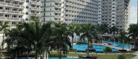 A hotel with multiple floors, a swimming pool area with palm trees, and a children's play area.