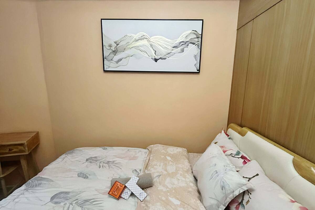 Une chambre à coucher avec un lit, une tête de lit en bois, un tableau accroché au mur et une petite table en bois.