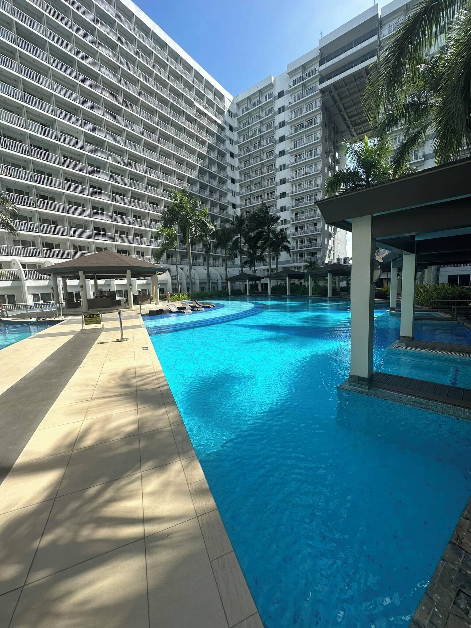A swimming pool with a tiled deck, surrounded by a multi-story building with balconies.