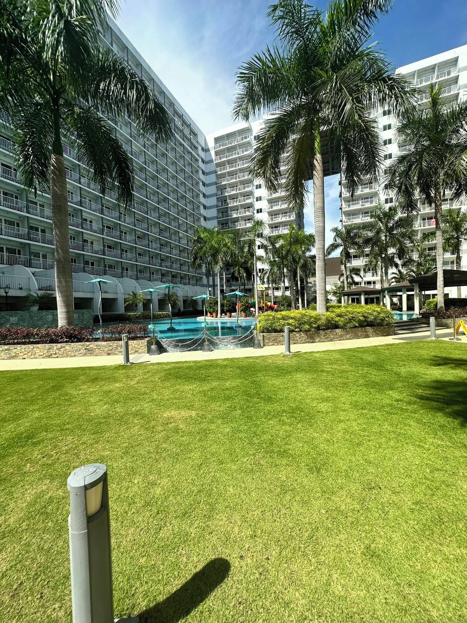 Un hotel moderno con diversi piani, una piscina e palme.