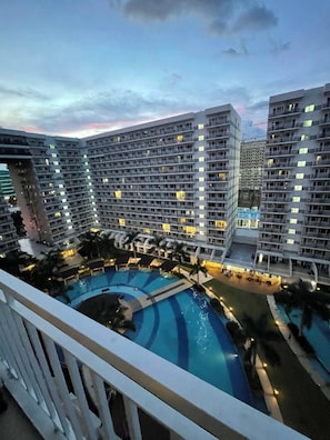 Un hotel moderno de gran altura con varios balcones, una piscina central y palmeras alrededor.