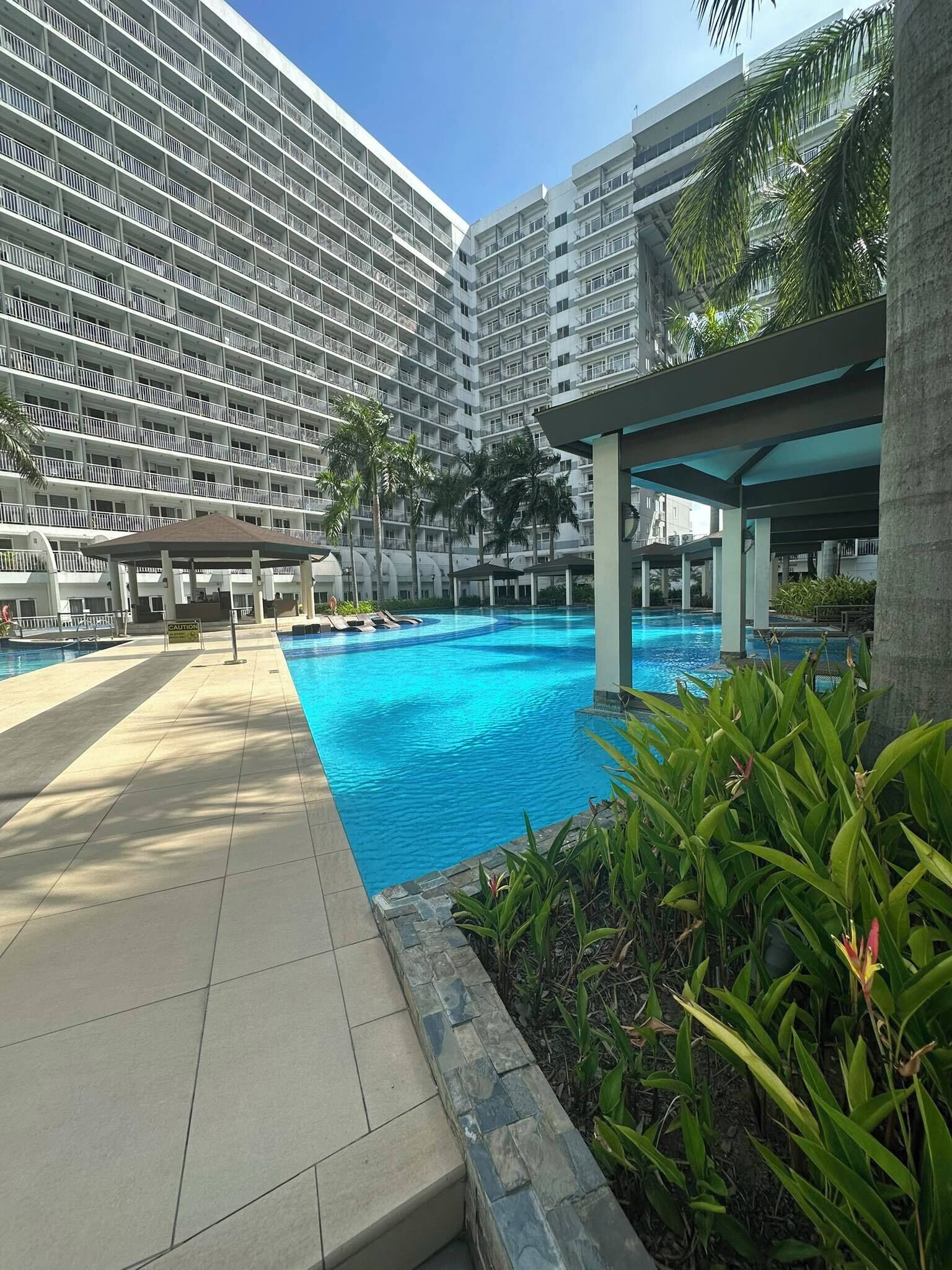 Un hôtel moderne doté d’une grande piscine, de nombreux balcons et d’une végétation luxuriante.