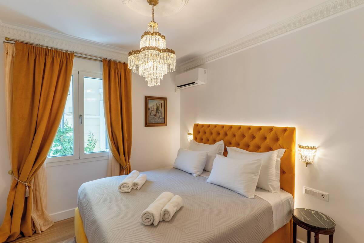 A neatly made bed with rolled towels, a chandelier, and a picture on the wall.