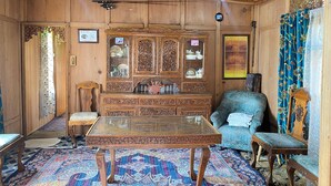 Una habitación tradicional con techo de madera, una mesa con cubierta de vidrio, un sofá azul y una alfombra estampada.