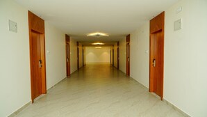 Un largo pasillo estrecho con puertas de madera a ambos lados, que conduce a una habitación luminosa al final.