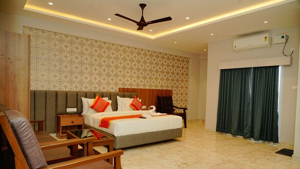Habitación de hotel con cama, escritorio, silla, ventilador de techo y ventana con cortinas.
