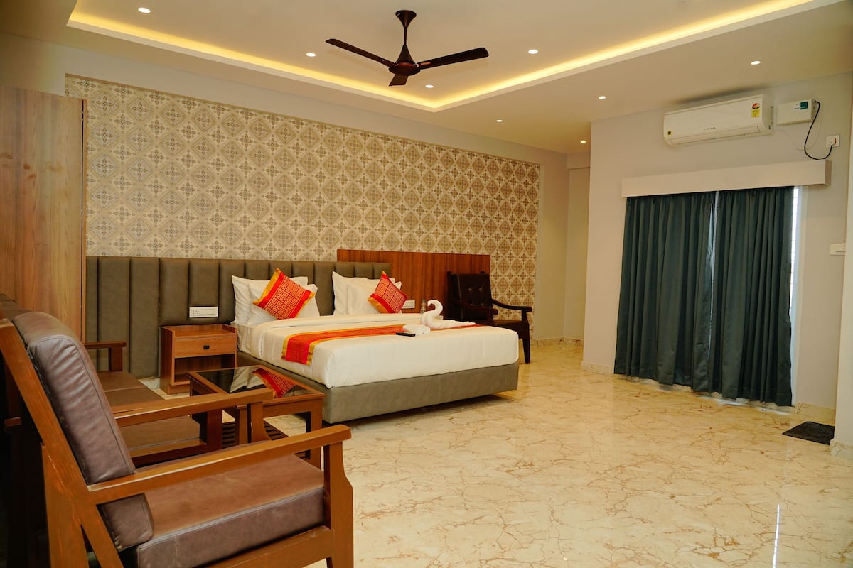 Quarto de hotel com cama, escrivaninha, cadeira, ventilador de teto e janela com cortinas.