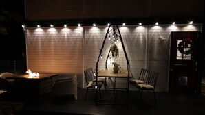 An outdoor patio with a table and chairs, a hanging light fixture, and a door with a wreath. - Welcome to my My Cozy Mushroom cottage ! (Big Bear)