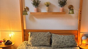 A bedroom with a wooden headboard, a bed with patterned bedding, a green blanket with red and white mushrooms, and a nightstand with a lamp and a bowl of mushrooms. - Welcome to my My Cozy Mushroom cottage ! (Big Bear)