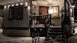 A snow-covered porch with a red door, outdoor lights, and potted plants. - Welcome to my My Cozy Mushroom cottage ! (Big Bear)