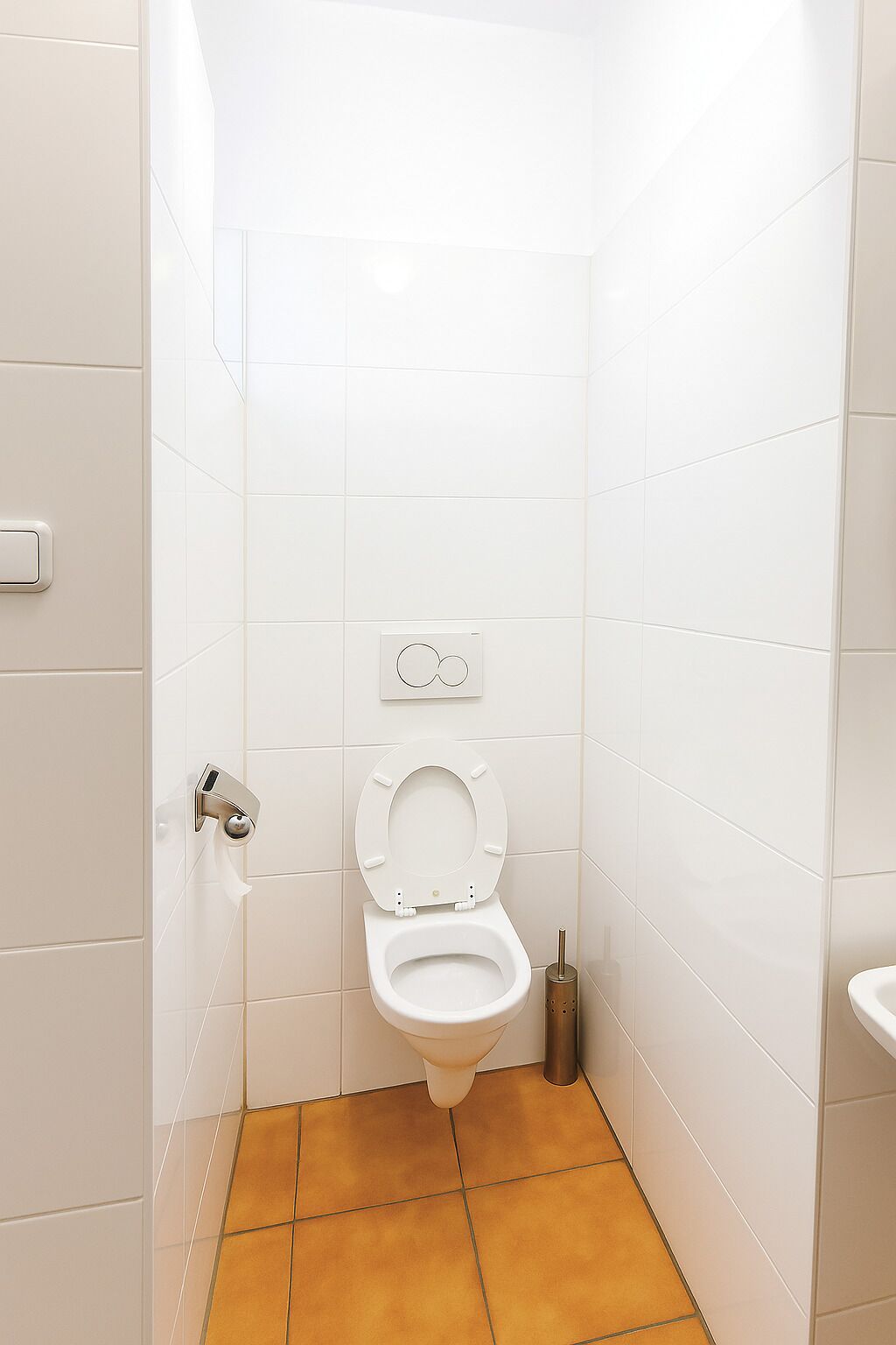 A small, white-tiled bathroom with a toilet, a bidet, and a wall-mounted flush handle.