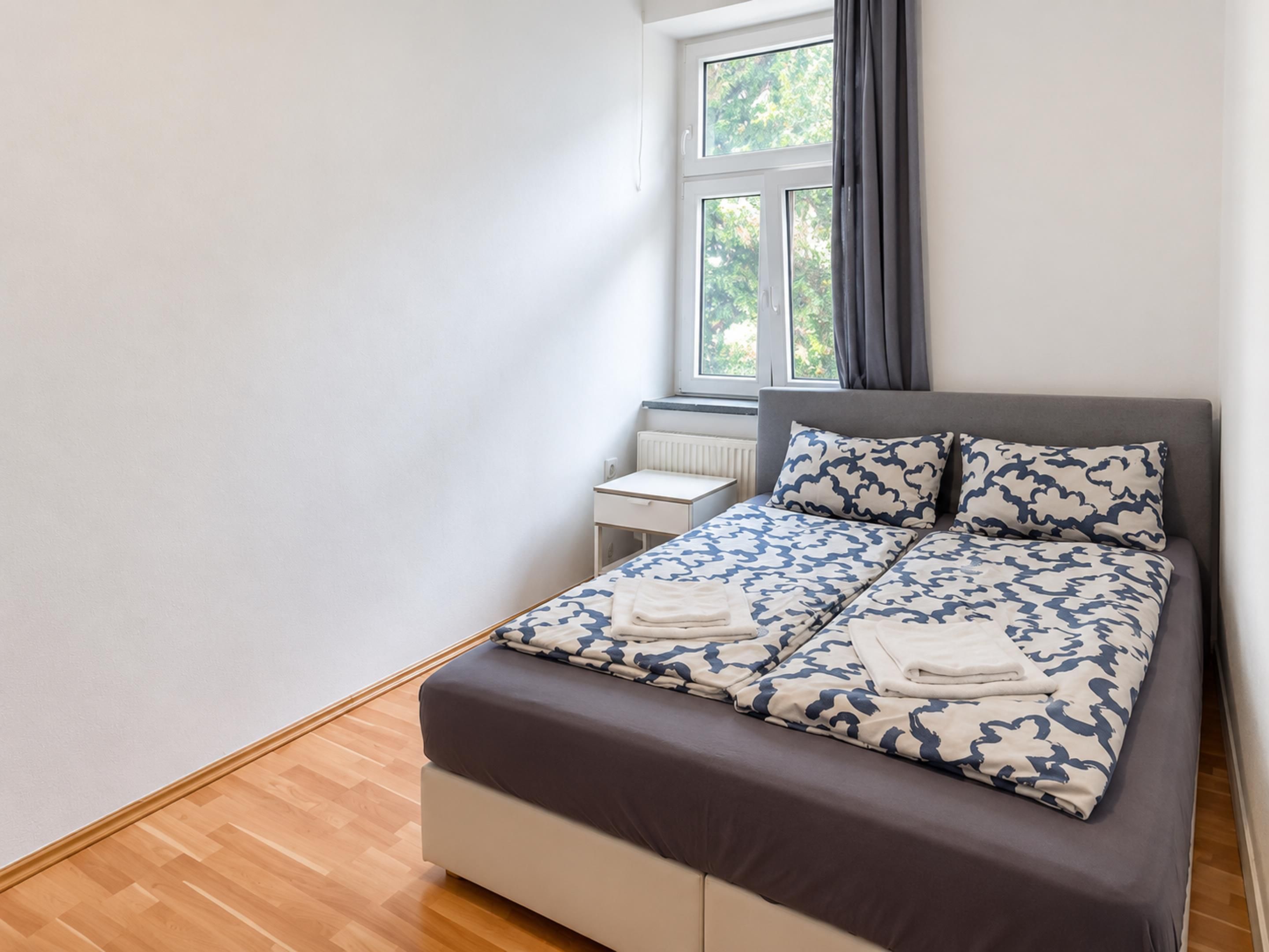 Een moderne slaapkamer met een bed, nachtkastje en een raam met gordijnen.
