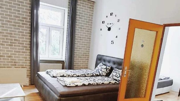 Un dormitorio con cama, suelo de madera, ventana y un reloj en la pared.
