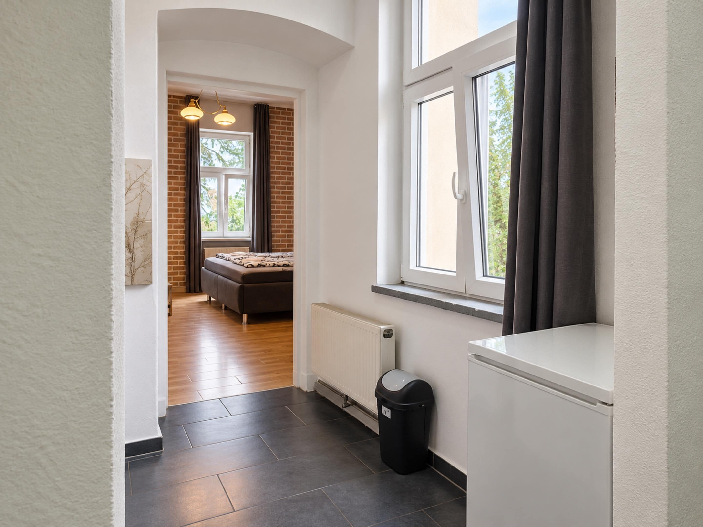 Ein modernes Interieur mit einem Bett, einem Heizkörper, einem Mülleimer und einem Vorhangfenster.