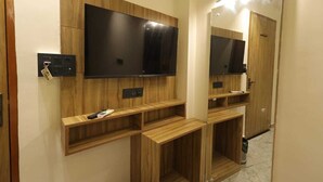 Baño con muebles de madera, un televisor de pantalla plana montado en la pared y un espejo con luces superiores.