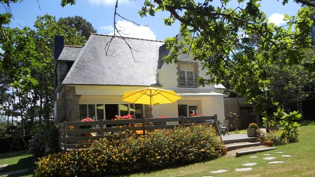 Una casa a due piani con un balcone, un ombrello giallo e un giardino con lastre di pietra.