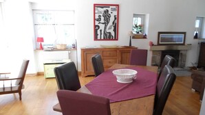 Zona pranzo con tavolo in legno, sei sedie, tovaglia rossa, colander bianco, camino e un'opera d'arte incorniciata appesa al muro.