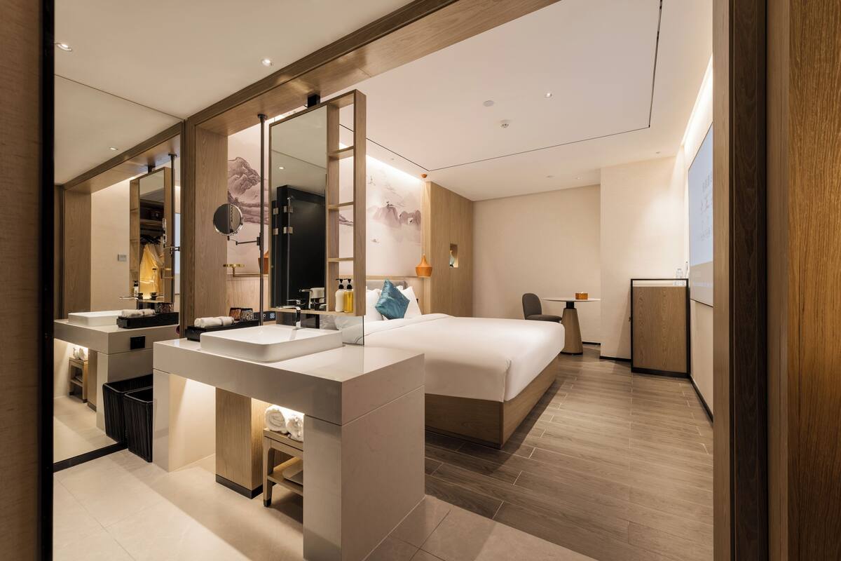 Een moderne hotelkamer met een groot bed, een aparte badkamer met wastafel en een bureau.