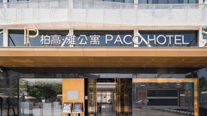 La entrada del PACOHOTEL, con un letrero llamativo, puertas de vidrio y el reflejo de la fachada del edificio.
