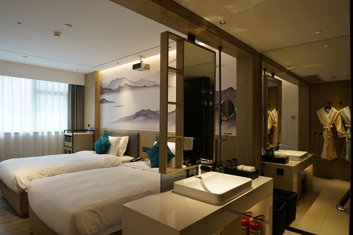 Een moderne hotelkamer met twee bedden, een grote spiegel, een badkamer met een wastafel en uitzicht op bergen vanuit het raam.
