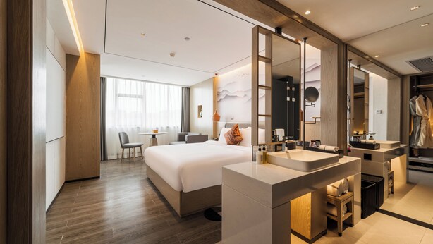 Habitación de hotel moderna con una cama grande, un área de baño separada y un escritorio con una silla.