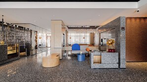 Un vestíbulo moderno con un muro de cristal que exhibe diversos objetos, una zona de estar con una silla azul y una pared decorativa con un tocadiscos.