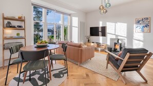 A modern living room with a fireplace, a TV, and a dining area with a table and chairs. - Loughrigg at Lipwood House (Windermere)