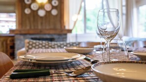 A dining table set with plates, cutlery, and a wine glass, with a patterned tablecloth and a wooden wall with a decorative light fixture in the background. - Spacious 4BDR/9P apt at the foot of the ski slopes (Megève)