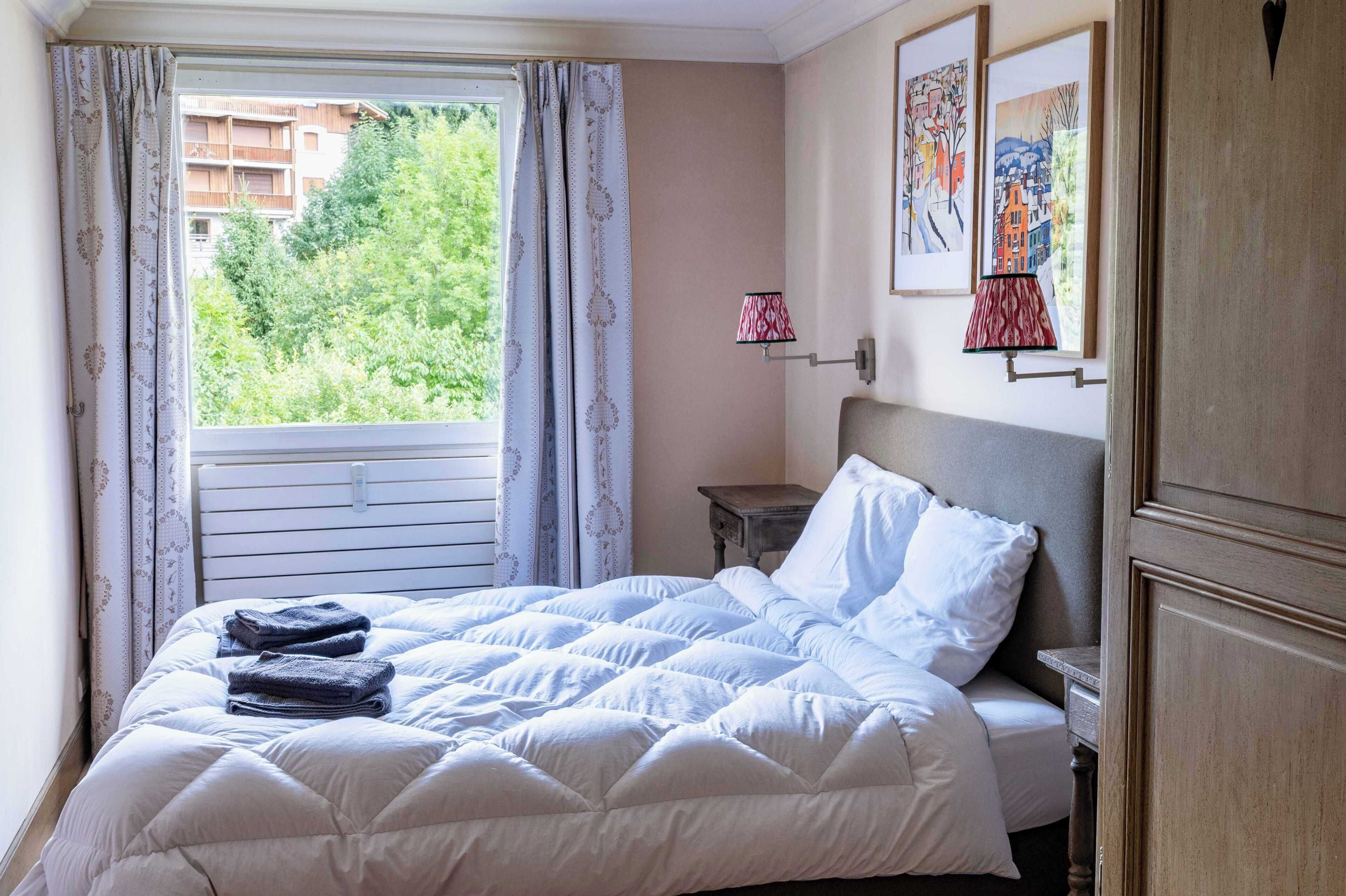 Um quarto com cama, mesa de cabeceira, abajur e janela com cortinas.