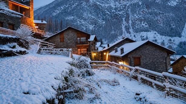 Un village de montagne enneigé, avec des bâtiments en pierre et un escalier en bois.