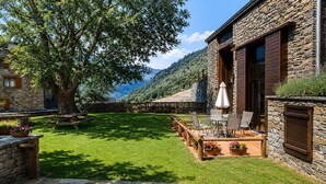 Un bâtiment en pierre doté d’une terrasse, de sièges en plein air et d’un grand arbre.
