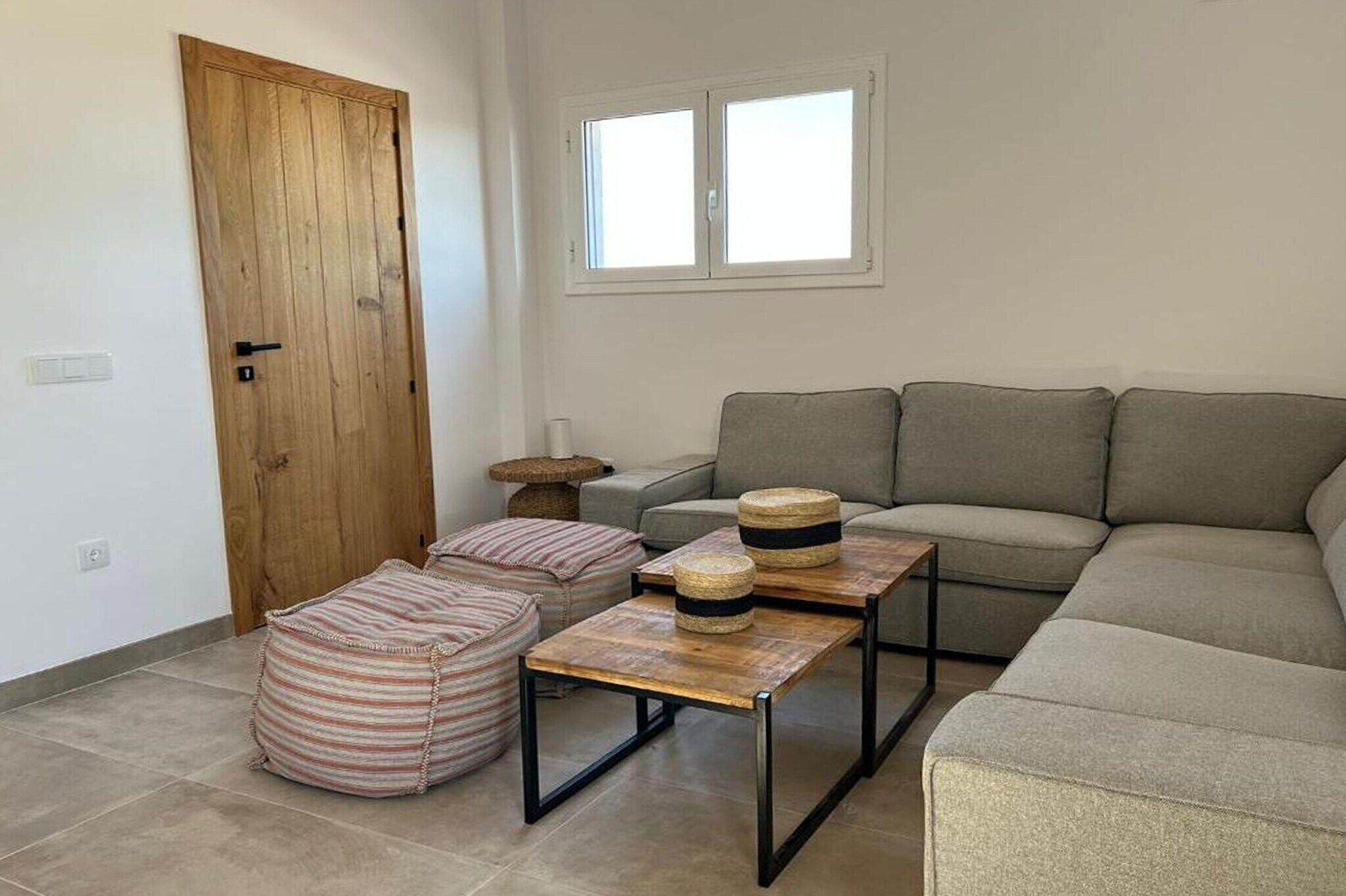 Un salon comprenant un canapé, deux poufs, une table basse et une porte en bois.