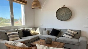 Een moderne woonkamer met een grijze modulaire bank, rieten stoelen, een houten salontafel en een grote ronde wanddecoratie van geweven materiaal.