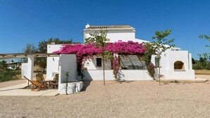 Een wit gebouw met een overdekte patio en een pergola vol roze bloemen.
