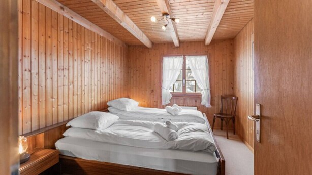 Dormitorio con paneles de madera, una cama, una silla y una ventana con cortinas.