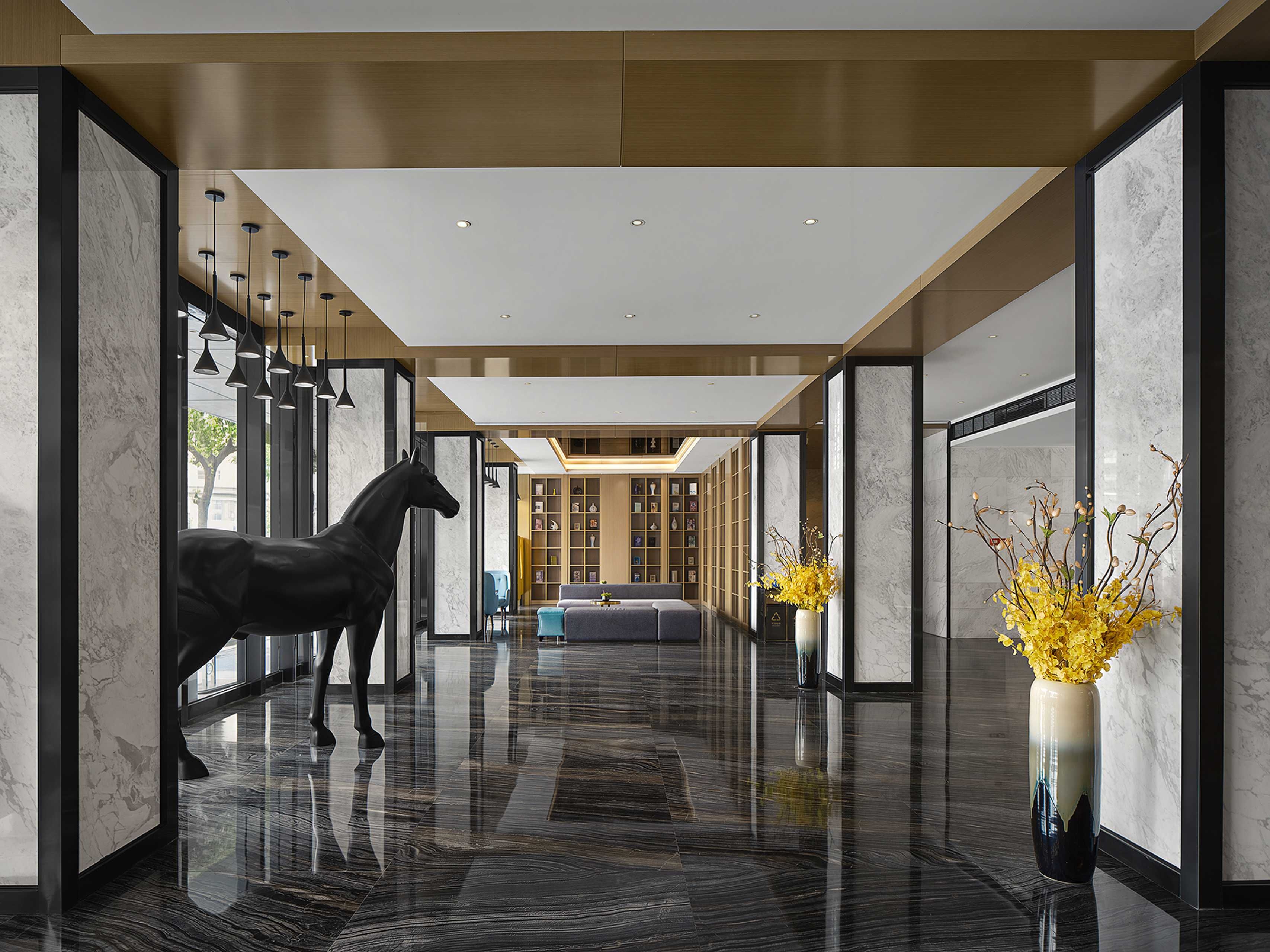 A modern hotel lobby with a polished marble floor, a horse statue, and a vase with yellow flowers.